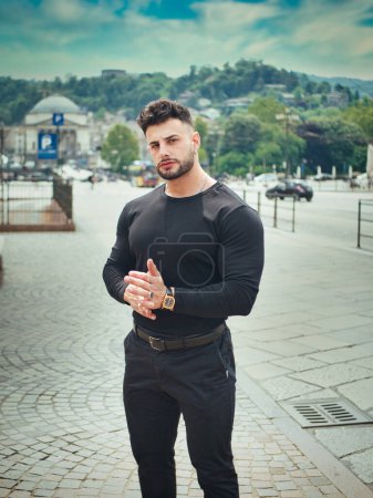 Atractivo atlético hombre warlking alrededor del centro de la ciudad europea, con camisa y pantalones negros