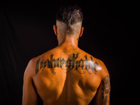 Foto de Close-up of back of unrecognizable shirtless muscular man, standing, in studio shot against black background - Imagen libre de derechos