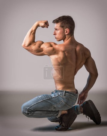 Téléchargez les photos : Young bodybuilder in kneeling pose in studio shot, shirtless, wearing jeans - en image libre de droit