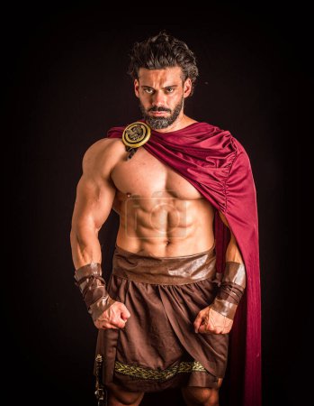 Photo for Handsome muscular man posing in roman or spartan gladiator costume with shield and sword, isolated on black background in studio - Royalty Free Image