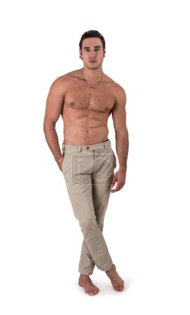 Full figure shot of handsome shirtless athletic young man in pants, looking at camera in studio shot, isolated on white background