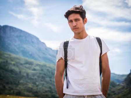 Foto de Guapo joven senderismo en exuberante paisaje de montaña verde mirando a la cámara - Imagen libre de derechos