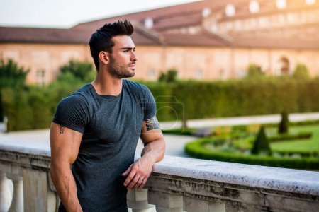 Schöner muskulöser Mann mit Tätowierung posiert im europäischen Luxusgarten in Turin, Italien