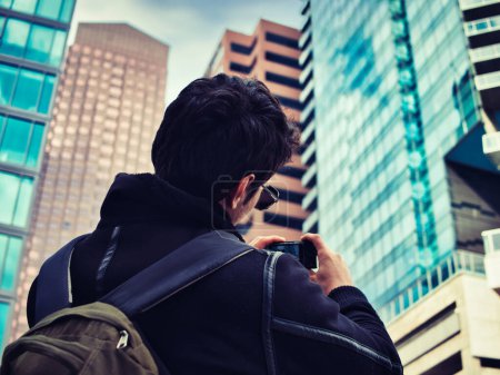 Téléchargez les photos : Jeune homme prenant des photos avec smartphone dans la ville moderne, en hiver ou en automne, vu de dos - en image libre de droit