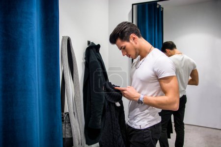 Photo for Young Handsome Man Trying on Clothes in Clothing Stores Changing Room in Front of a Mirror or in Room Closet - Royalty Free Image