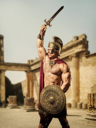 Photo for Young handsome muscular man posing in roman or spartan gladiator costume with sword on ancient ruins in Rome - Royalty Free Image