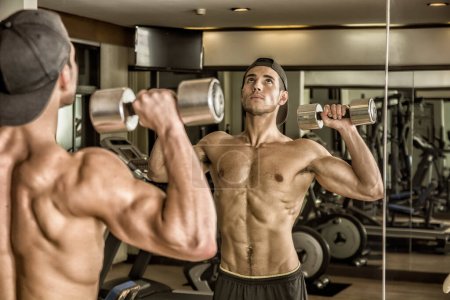 Photo for Handsome shirtless muscular young man exercising shoulders in gym with dumbbells - Royalty Free Image