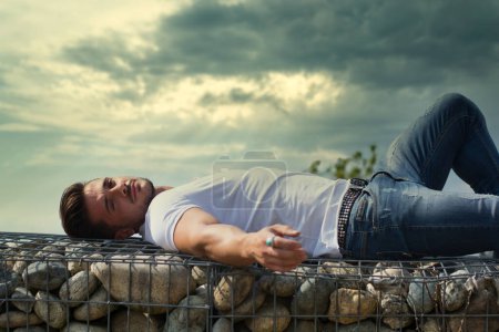 Photo for Handsome young man lying down on stone blocks, looking at camera - Royalty Free Image
