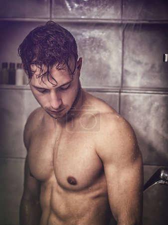 Nackter, athletischer junger Mann duscht im Badezimmer, um sich zu erfrischen und deckt die Leiste mit der Hand ab
