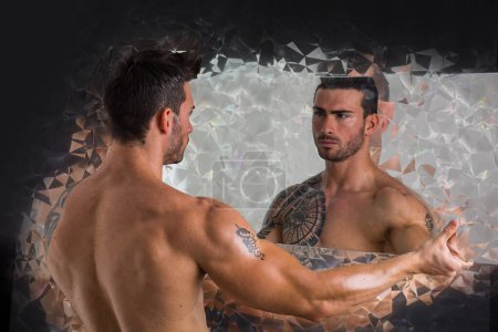 Foto de Un hombre atractivo musculoso sin camisa parado junto a un espejo, mirando su propio reflejo - Imagen libre de derechos