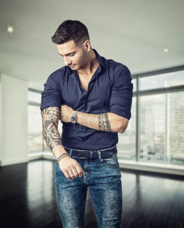 Un hombre con un tatuaje en el brazo de pie en la bonita sala de estar, en casa
