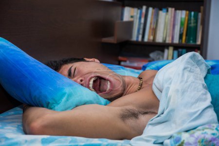 Téléchargez les photos : Un homme couché au lit, la bouche ouverte, hurlant à cause d'un cauchemar - en image libre de droit