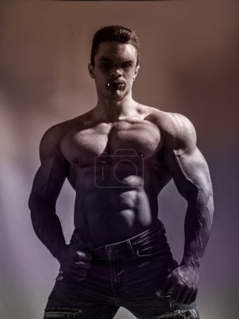Photo for Portrait of a Young Muscular Vampire Man Shirtless, Showing his Torso, Chest and Abs, Looking at the Camera, on Dark Background for Halloween - Royalty Free Image