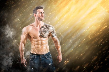 Photo for A man with a tattoo on his arm standing in the rain. Photo of a tattooed man standing in a rain of sparks and lights, showcasing his muscular physique - Royalty Free Image