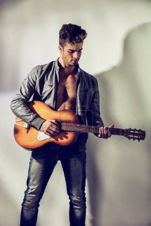 Foto de Un hombre sin camisa con una chaqueta abierta en el torso desnudo, sosteniendo una guitarra naranja - Imagen libre de derechos