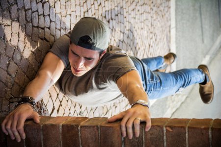 Téléchargez les photos : Un jeune homme pendu à un mur de briques. Illusion optique prise - en image libre de droit