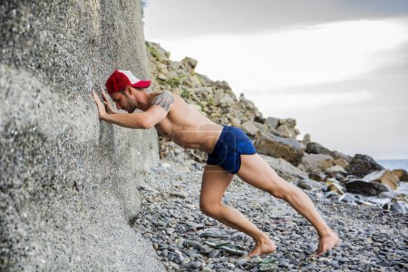 Photo for A shirtless muscular man doing stretching exercise on the beach - Royalty Free Image