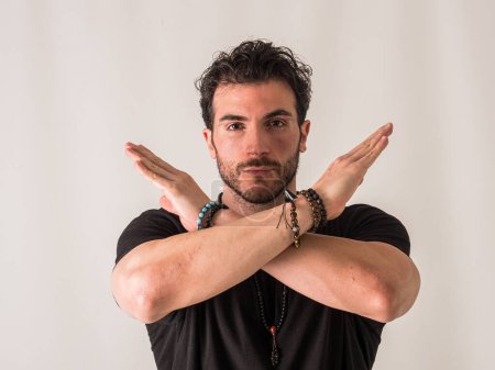 Photo for A man wearing a black shirt and bracelets, making an X sign with his arms, looking at camera - Royalty Free Image