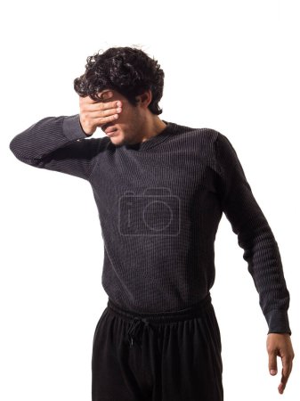 Foto de Un joven vistiendo un suéter negro y pantalones negros cubriendo los ojos con su mano, sin querer ver - Imagen libre de derechos