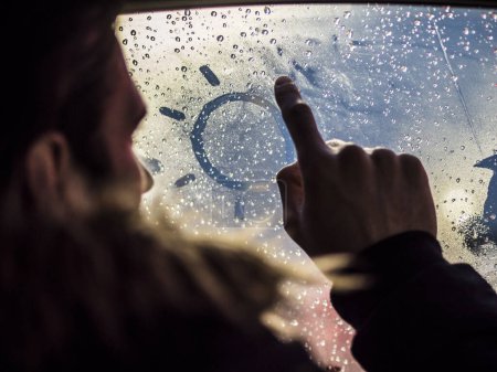 Foto de Una persona está mirando por la ventana de un coche y dibujando un sol en el vidrio empañado - Imagen libre de derechos