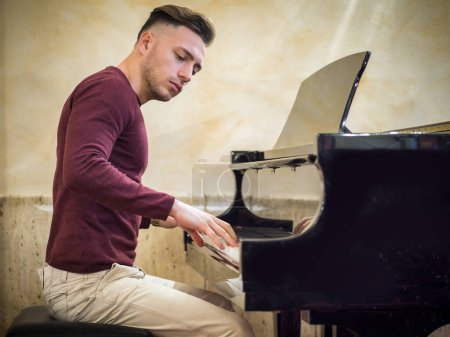 Téléchargez les photos : Jeune bel artiste masculin jouant son piano classique en bois, portrait d'intérieur - en image libre de droit