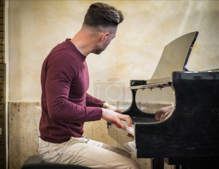 Téléchargez les photos : Jeune bel artiste masculin jouant son piano classique en bois, portrait d'intérieur - en image libre de droit