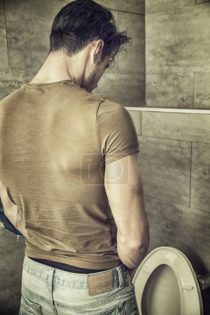 Rear View of a Young Man in Black Outfit Peeing at the Toilet Inside his Bathroom.