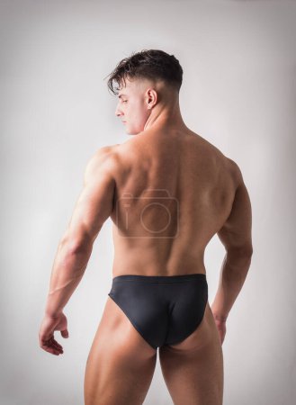 Rückansicht von Young Gym Fit Man zeigt seinen sexy Rücken, während er zur Seite schaut. auf hellem Hintergrund im Studio