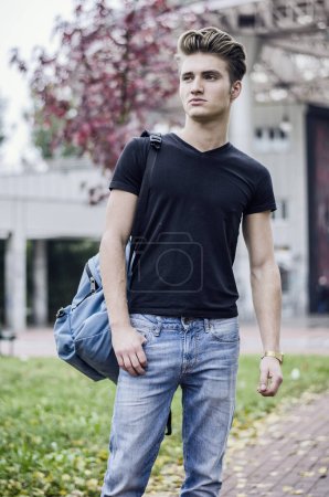 Foto de Atractivo joven de pie en el entorno de la ciudad, con mochila en un hombro - Imagen libre de derechos