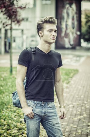 Foto de Atractivo joven de pie en el entorno de la ciudad, con mochila en un hombro - Imagen libre de derechos