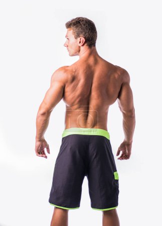 A man with no shirt on is depicted standing in front of a white background in this photo. His stance is confident and he gazes directly at the camera.