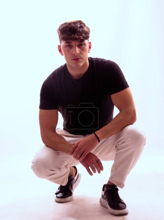 A man is captured in a photograph as he kneels down wearing a black shirt and white pants. The simple yet striking contrast between his clothing is highlighted in the image.