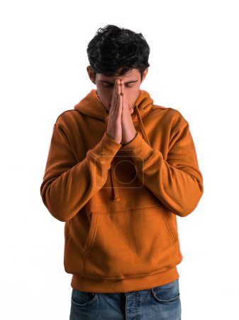 Ein Mann mit orangefarbenem Kapuzenpullover bedeckt sein Gesicht mit den Händen und verschleiert seine Gesichtszüge in einer Geste der Anonymität oder Bedrängnis.