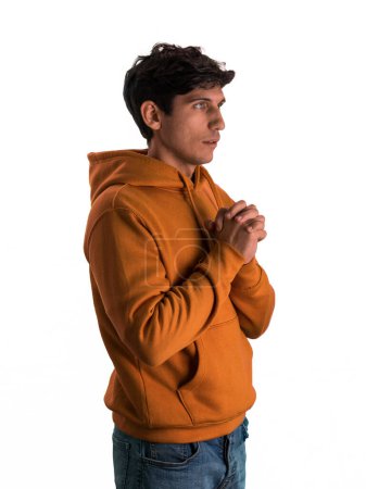 A man wearing an orange hoodie is shown bowing his head and clasping his hands in prayer. He appears focused and reverent in his solemn act of devotion.