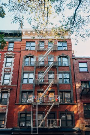 Foto de Exterior de un apartamento típico de Nueva York con escalera de incendios en la parte delantera, árbol en frente. - Imagen libre de derechos
