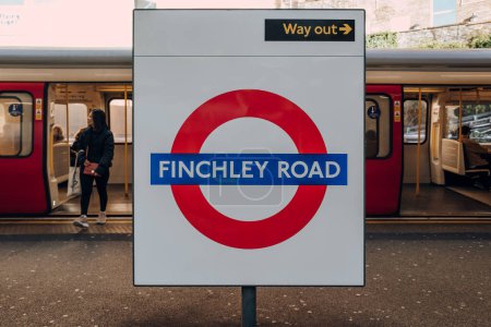Foto de Londres, Reino Unido - 26 de diciembre de 2022: signo de nombre Roundel en la plataforma al aire libre de la estación de Finchley Road del metro de Londres, el tren subterráneo más antiguo del mundo, tren detrás, enfoque selectivo. - Imagen libre de derechos