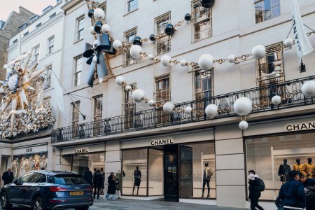 Foto de Londres, Reino Unido - 26 de diciembre de 2022: Collar gigante Decoración de Navidad en el exterior de la tienda Chanel en New Bond Street, una de las calles más famosas para ir de compras de lujo en Londres, la gente pasa caminando.. - Imagen libre de derechos