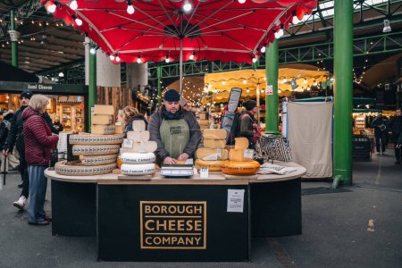 Téléchargez les photos : London, UK - January 27, 2023: Man working at a Borough Cheese Company stall in Borough Market, one of the largest and oldest food markets in London. - en image libre de droit