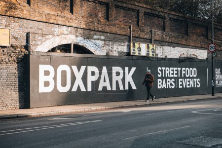 Photo for London, UK - February 09, 2023: Sign for Boxpark Shoreditch, a shipping container mall for independent fashion and lifestyle stores and cafes, man walking past. - Royalty Free Image