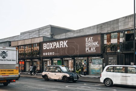 Photo for London, UK - February 09, 2023: Taxi in front of shops at Boxpark Shoreditch, London, shipping container pop-up mall for independent and fashion and lifestyle stores and cafes. - Royalty Free Image