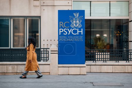 Foto de London, UK - February 09, 2023: Sign at the entrance to The Royal College of Psychiatrists, the main professional organisation of psychiatrists in the United Kingdom, woman walking past. - Imagen libre de derechos