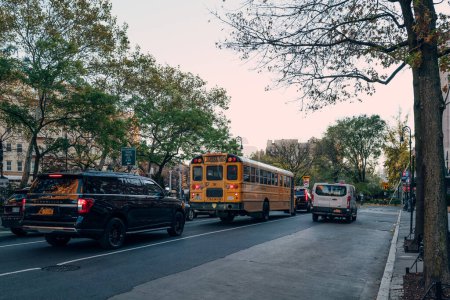 Foto de New York, USA - November 22, 2022: Yellow school bus amongst the cars on a road in Manhattan, New York. The City of New York provides student with free transportation to and from school. - Imagen libre de derechos