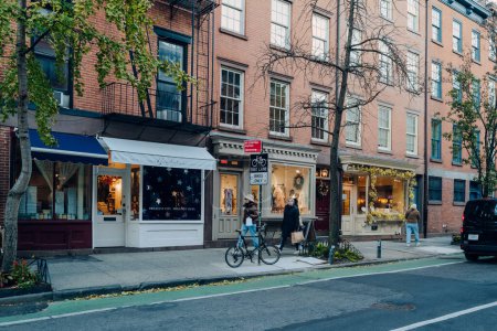 Photo for New York, USA - November 21, 2022: Row of shops on a street in West Village, a charming area of Manhattan famous for its shops and restaurants, women walking past. - Royalty Free Image