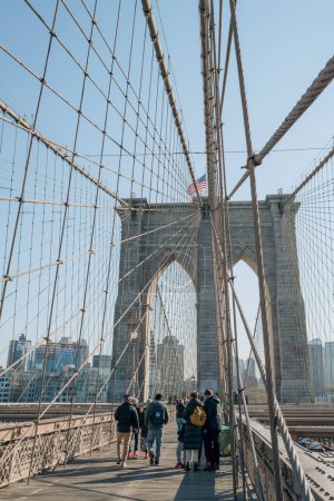 Téléchargez les photos : New York, USA - November 21, 2022: People walking on Brooklyn Bridge, a famous hybrid cable-stayed-suspension bridge in New York City, on a sunny winter day. - en image libre de droit