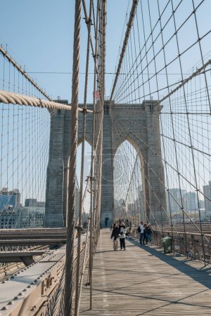 Téléchargez les photos : New York, USA - November 21, 2022: People walking on Brooklyn Bridge, a famous hybrid cable-stayed-suspension bridge in New York City, on a sunny winter day. - en image libre de droit