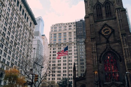 Photo for New York, USA - November 25, 2022: American flag on a pole by the Trinity Church in Financial District,  New York's financial heart and a home to Wall Street. - Royalty Free Image