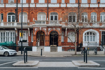 Téléchargez les photos : Londres, Royaume-Uni - 21 février 2023 : Bâtiments extérieurs ou traditionnels en briques rouges avec des cadres de fenêtre blancs à Kensington et Chelsea, un quartier riche de l'ouest de Londres favorisé par les célébrités. - en image libre de droit