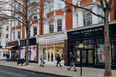 Téléchargez les photos : Londres, Royaume-Uni - 21 février 2023 : Rangée de magasins sur Sloane Street à Sloane Square, un quartier haut de gamme de Londres célèbre pour ses boutiques, sa culture et ses restaurants, les gens qui passent devant. - en image libre de droit