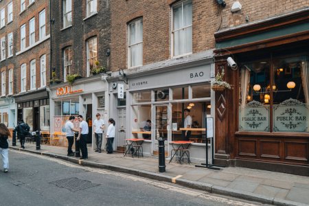 Téléchargez les photos : Londres, Royaume-Uni - 13 avril 2023 : Le personnel fume devant le restaurant taïwanais Bao à Soho, un quartier de Londres célèbre pour ses bars, restaurants et clubs LGBTQ +. - en image libre de droit