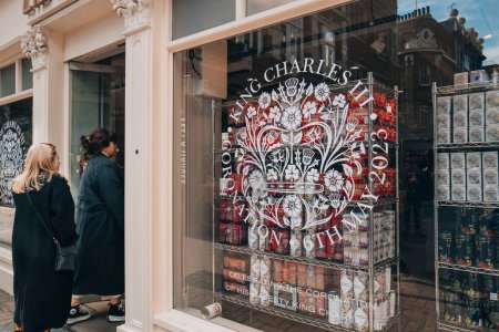 Téléchargez les photos : Londres, Royaume-Uni - 13 avril 2023 : Panneau célébrant le couronnement du roi Charles III à la fenêtre de Liberty, un grand magasin à Oxford Circus célèbre pour ses dessins Liberty, les gens entrant en arrière-plan. - en image libre de droit